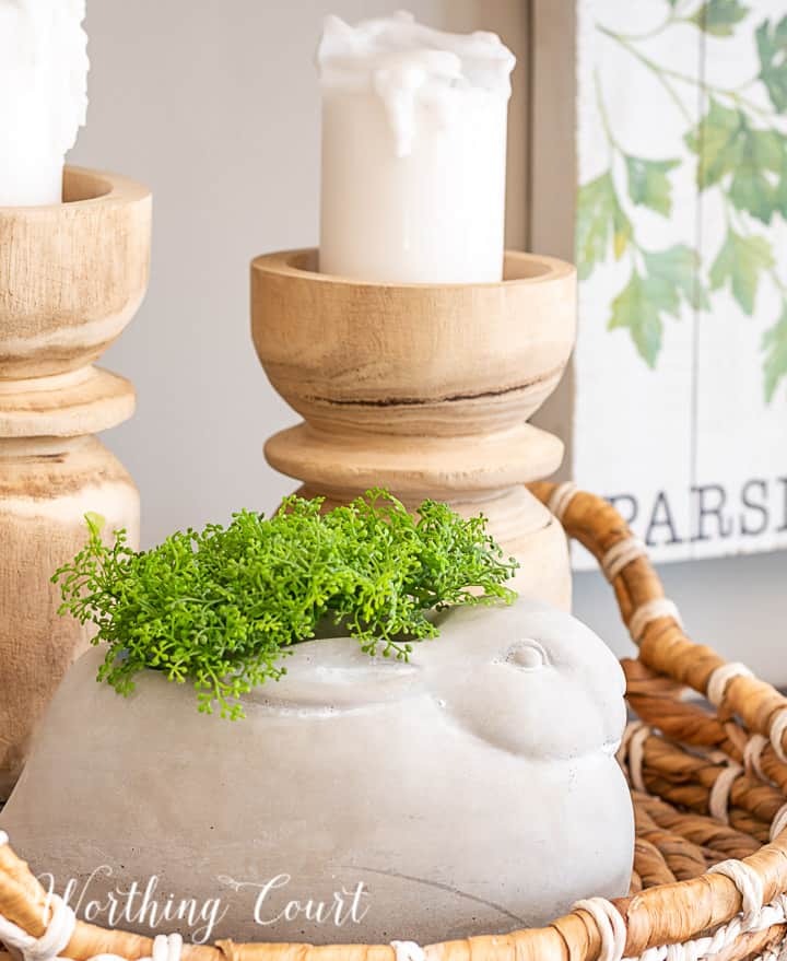 vignette with wood candlesticks and a concrete bunny in a round basket tray