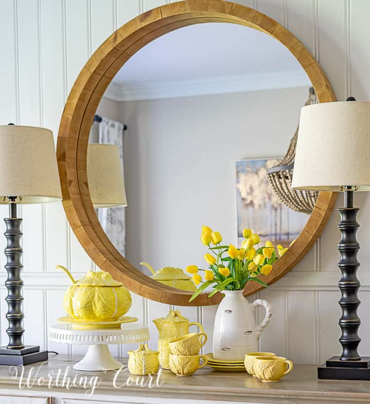 white sideboard with lamps and a round mirror above styled with yellow dishes for Easter