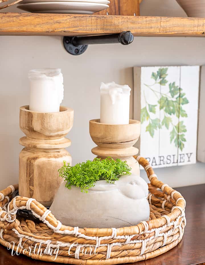 vignette with wood candlesticks and a concrete bunny in a round basket tray