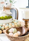 Easter centerpiece with white ceramic bunny in the middle of an egg wreath and a wood bowl filled with faux Easter eggs