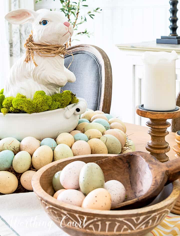 Easter centerpiece with white ceramic bunny in the middle of an egg wreath and a wood bowl filled with faux Easter eggs