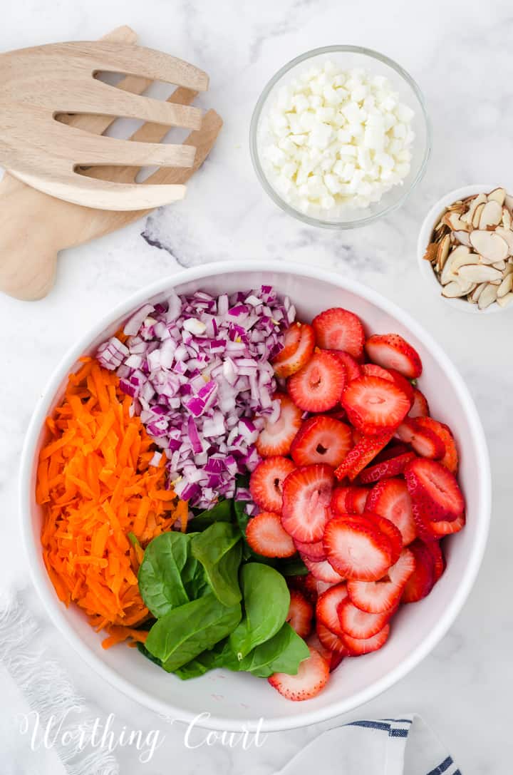 ingredients for a strawberry spinach salad in a white bowl