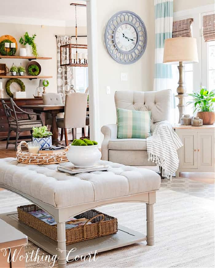 upholstered ottoman, gray tufted back recliner and blue and white curtains in the corner of a family room