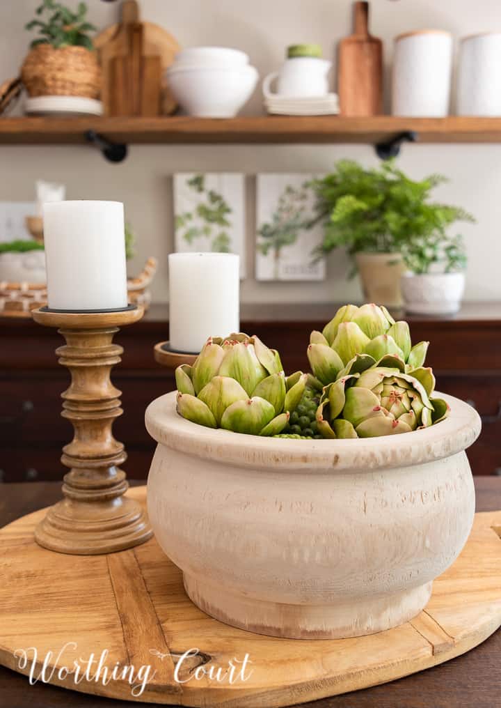 Centerpiece on a breadboard with a wooden bowl and wood candlesticks with shelves in the background