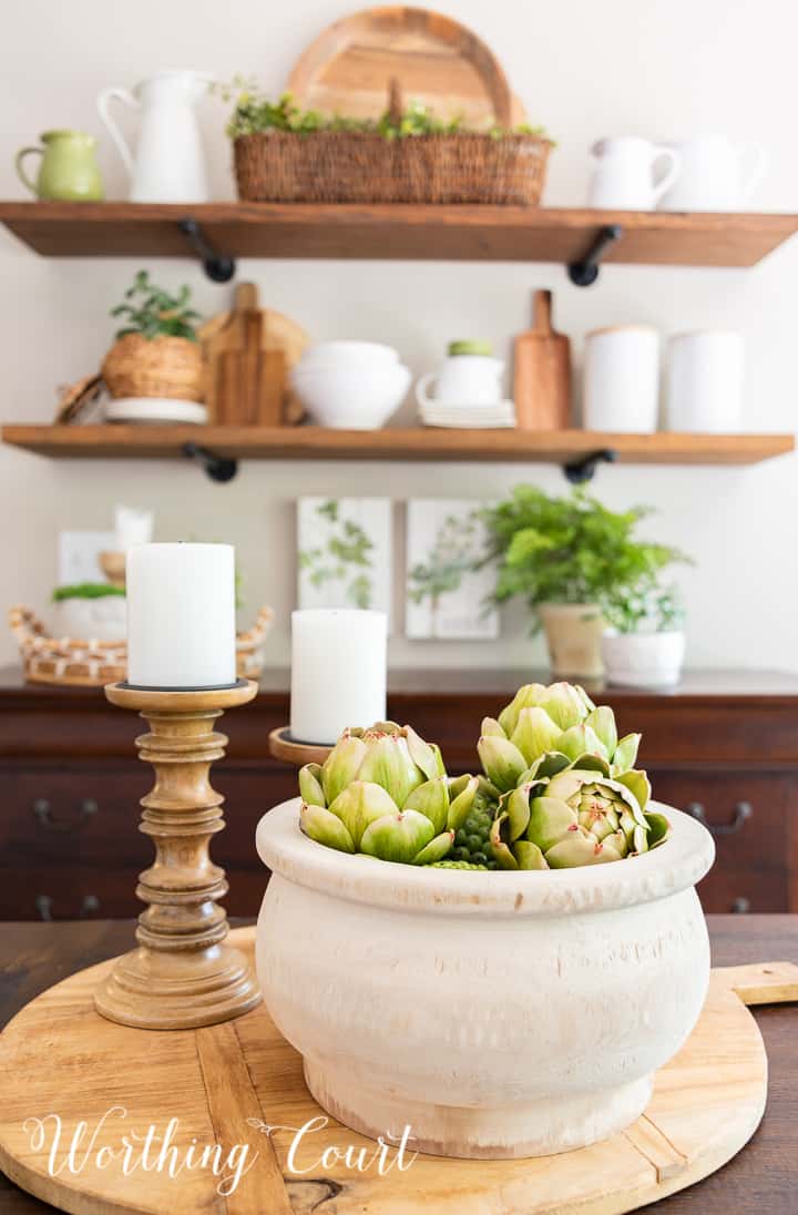 Centerpiece on a breadboard with a wooden bowl and wood candlesticks with shelves in the background