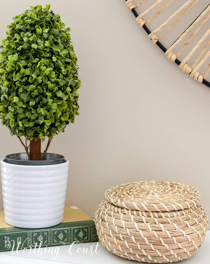 Summer mantel vignette with a candlestick, faux topiary and lidded wicker basket