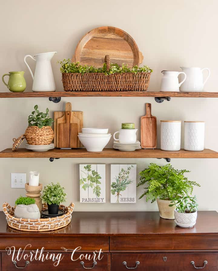 Open shelves decorated for summer with wood and white accessories and faux greenery.