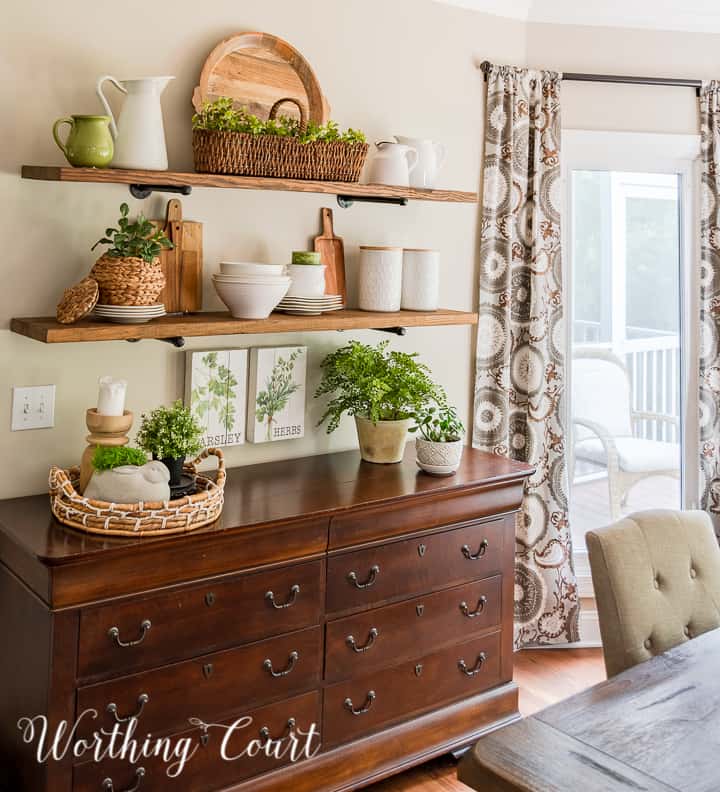 Open shelves decorated for summer with wood and white accessories and faux greenery.