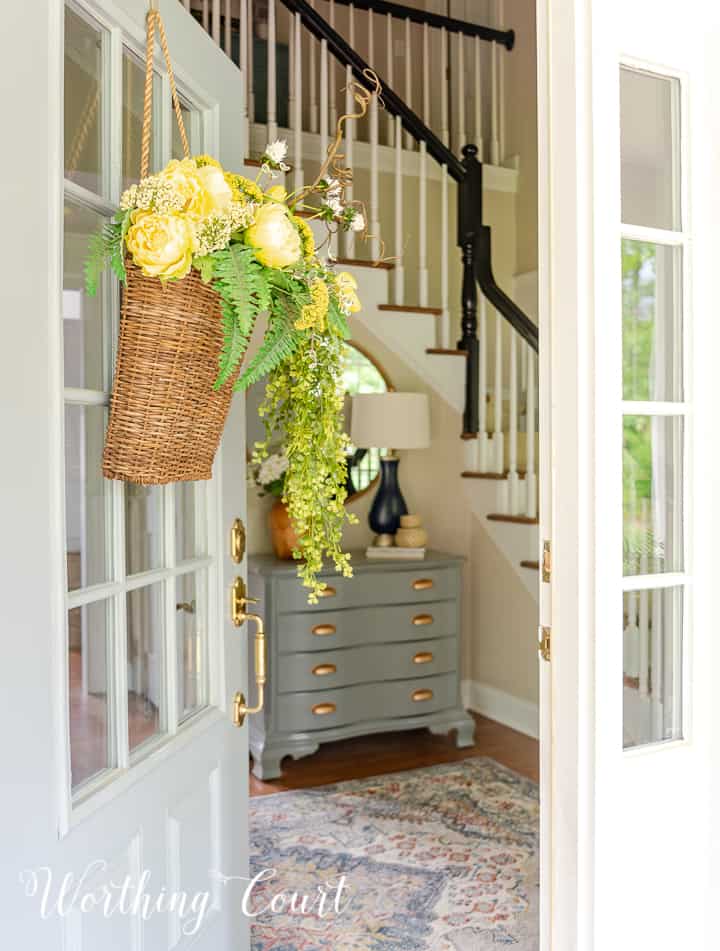 looking into a front door at a painted gray chest with gold handles and a round mirror