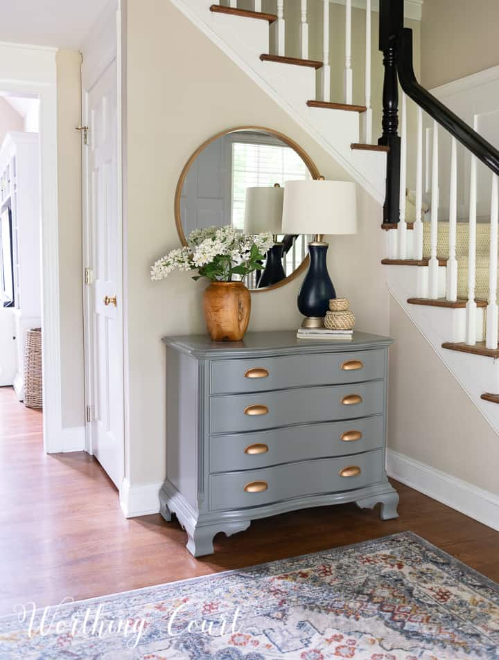 painted gray chest with gold handles and a round mirror