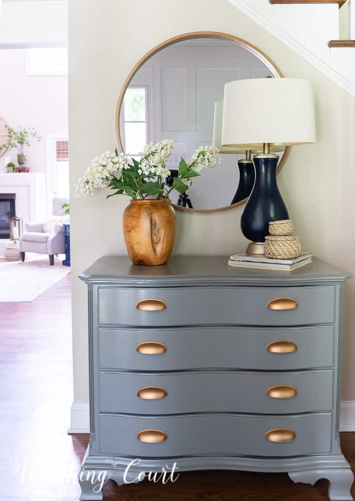 painted gray chest with gold handles and a round mirror