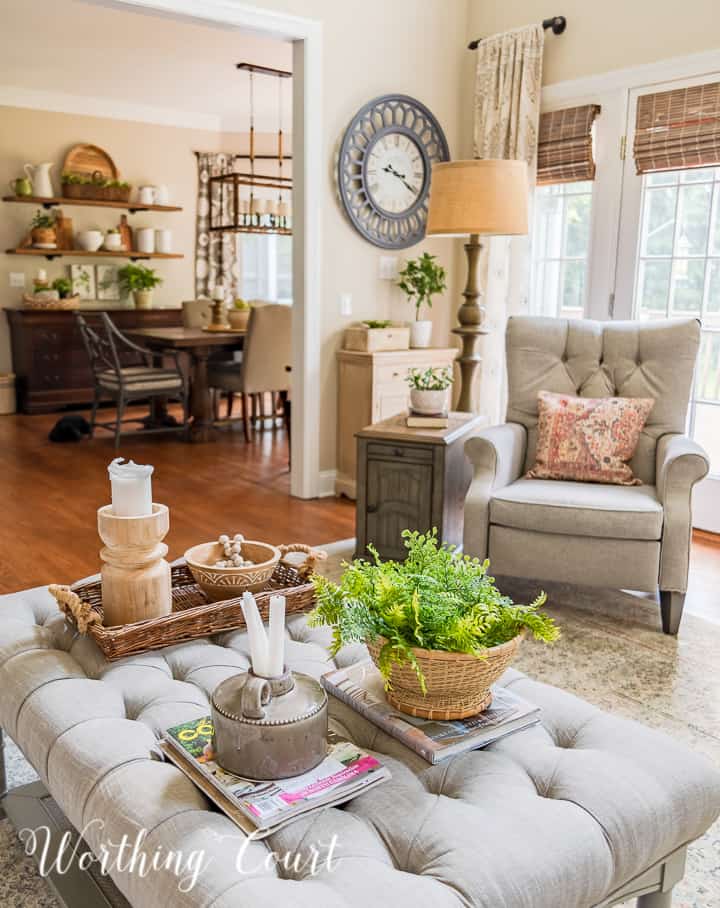 View of a family room with upholstered coffee table in foreground, tufted recliner and open shelves in the background