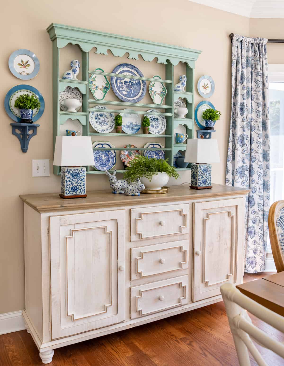 Beigefarbene Wände mit blauem Tellerregal, gefüllt mit blauem und weißem Frühlingsdekor, über einem weißen Sideboard
