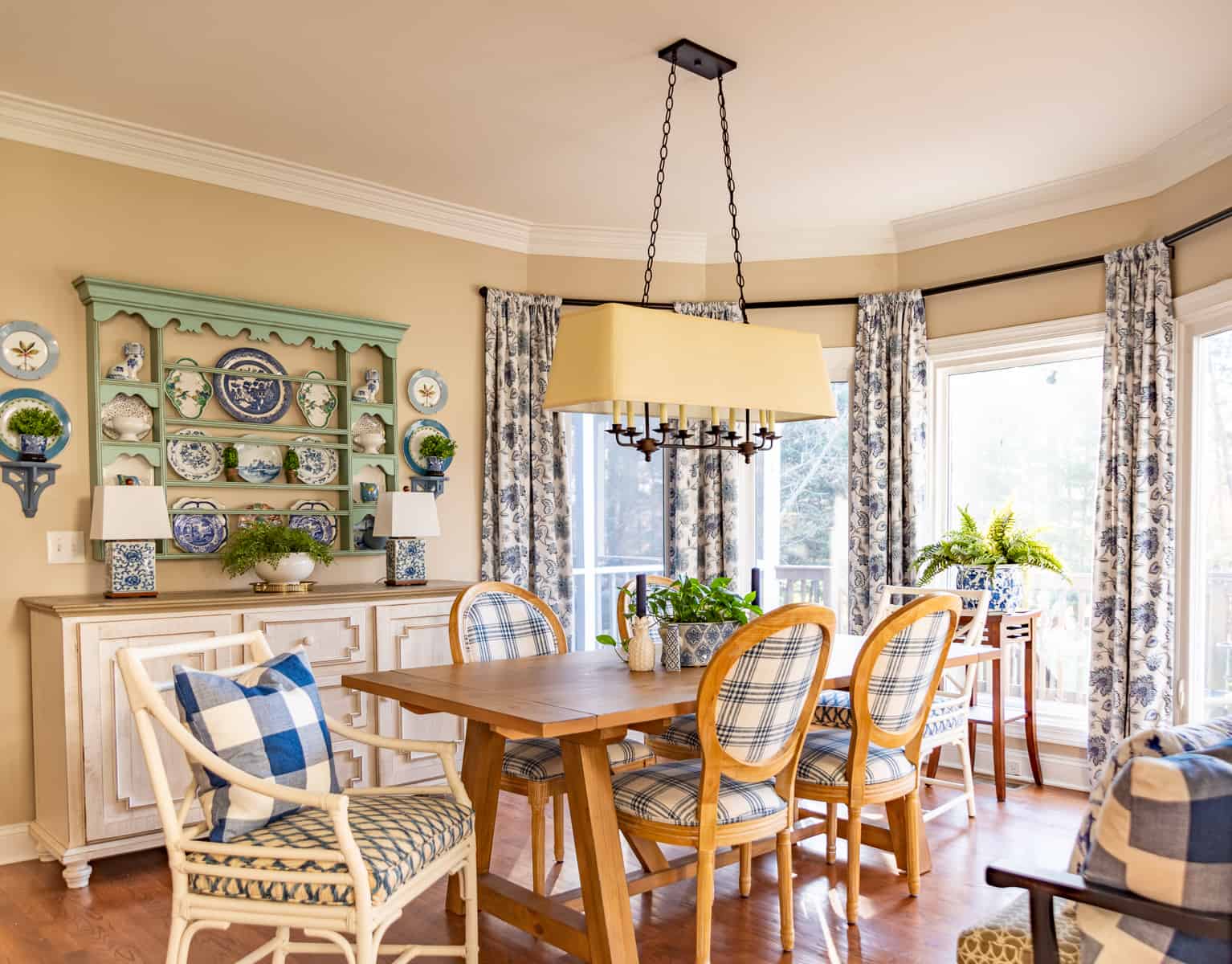 breakfast room with beige walls, pine table, blue and white chairs, blue plate rack above white sideboard with spring decorations