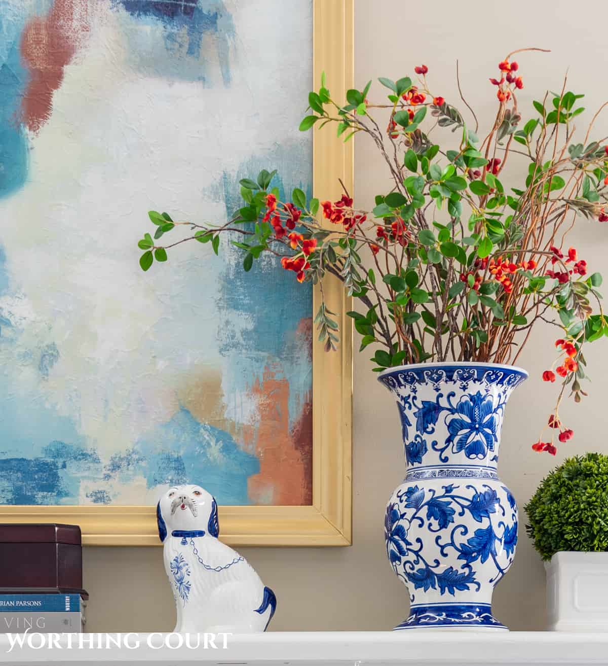 Blaue und weiße Vase auf Kaminsims mit Kunstgrün und Blumen vor einer beigen Wand