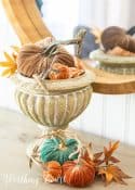 various colored velvet pumpkins and fall leaves in an urn and on the table surface