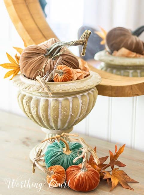various colored velvet pumpkins and fall leaves in an urn and on the table surface