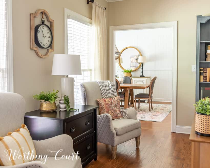 natural colored arm chair beside a black file cabinet with a view into the dining room in the background