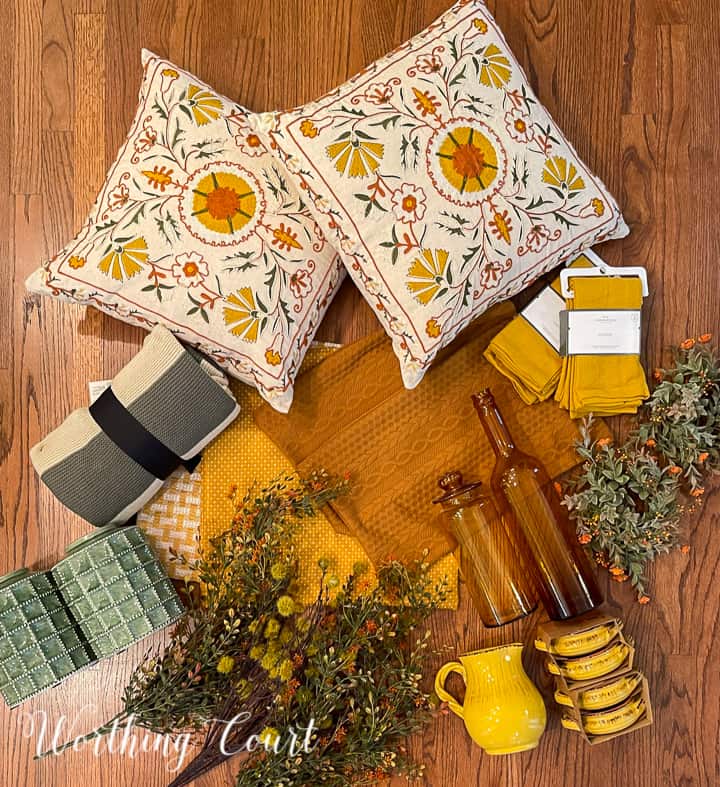 overhead view of fall decorations on a hardwood floor including pillows, foliage, dishes, pillow covers and a throw