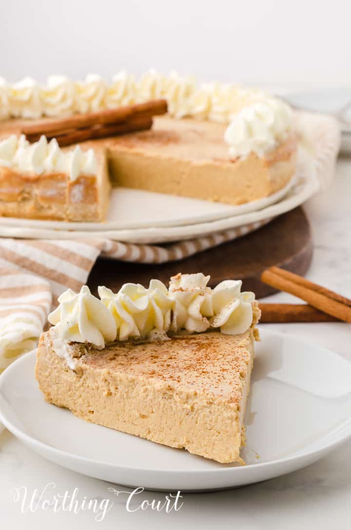 individual piece of gingerbread cheesecake with whipped topping garnish in front on whole cheesecake in the background