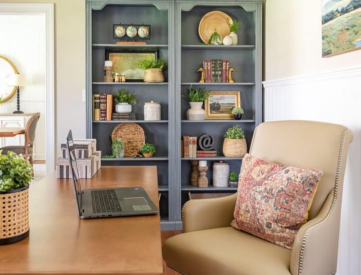 pair of gray bookcases filled with a variety of updated traditional accessories with a beige leather office chair in the foreground