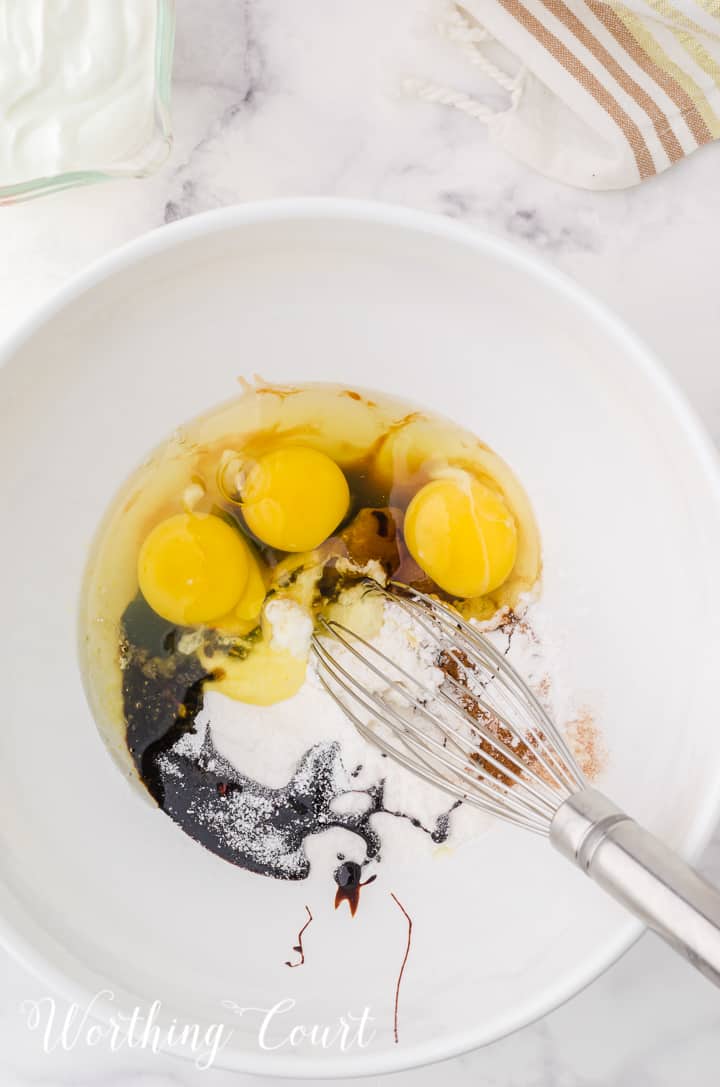 some of the ingredients for gingerbread cheesecake in a white mixing bowl with a whisk