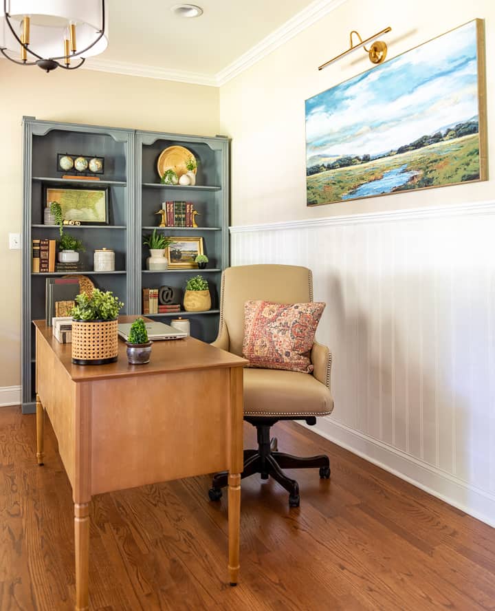 natural wood desk with beige leather chair and gray bookcases filled with accessories in background