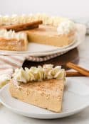 image of one piece of gingerbread cheesecake on a plate with rest of cheesecake in the background