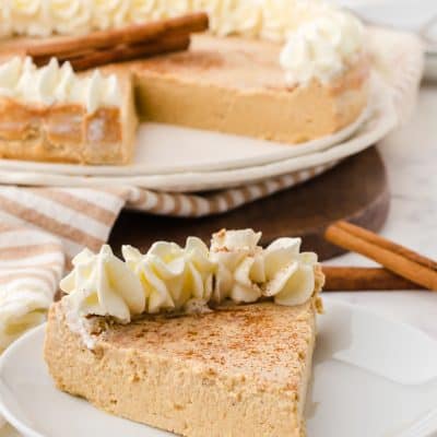 image of one piece of gingerbread cheesecake on a plate with rest of cheesecake in the background