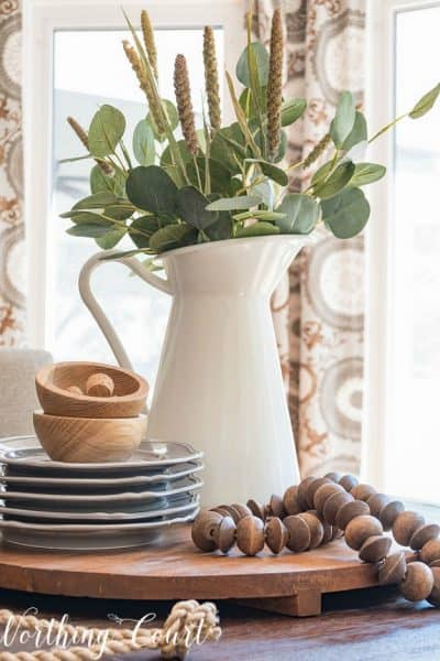 centerpiece on a round board with gray and wood accessories and eucalyptus stems in a white pitcher