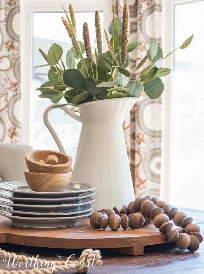 centerpiece on a round board with gray and wood accessories and eucalyptus stems in a white pitcher