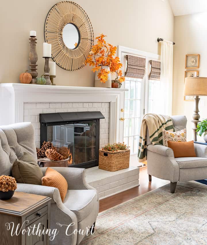 gray arm chairs, lamps and side tables beside white fireplace with fall decor on the mantel and hearth