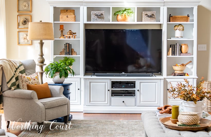 white entertainment center filled with tv and fall decor with a gray chair and coffee table in front