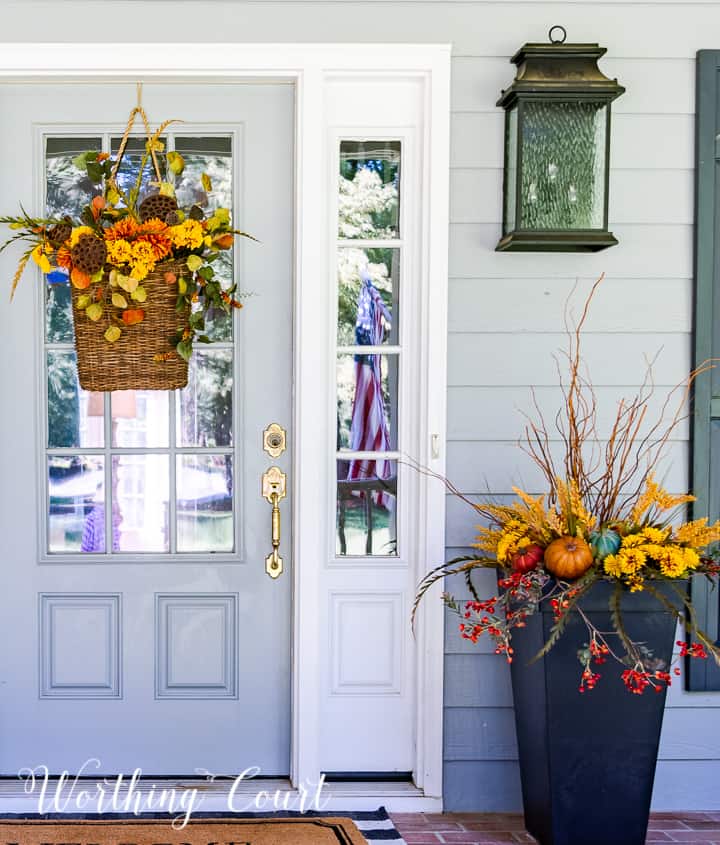 gray front door with a hanging basket and urn filled with faux fall stems and pumpkins in fall colors