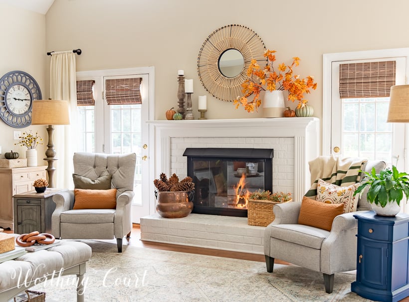 gray arm chairs, lamps and side tables beside white fireplace with fall decor on the mantel and hearth