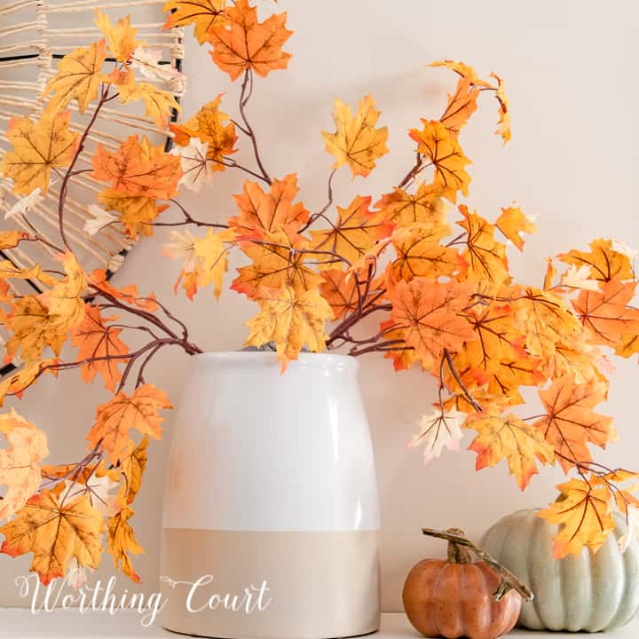 vase with fall leaf stems and two faux pumpkins on a white mantel