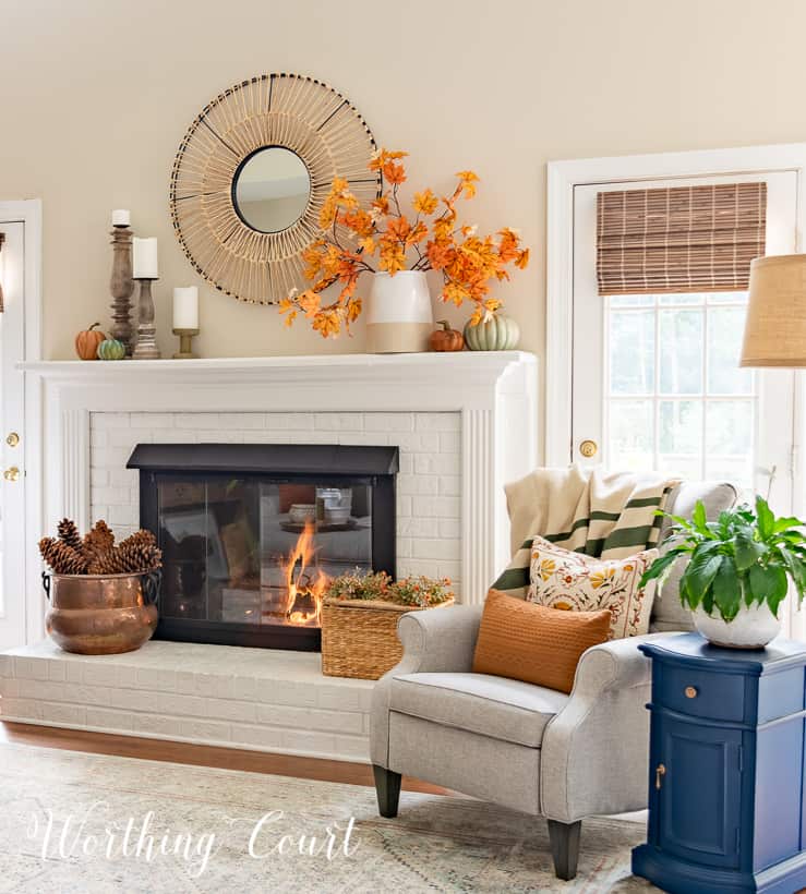 gray arm chair and side table beside white fireplace with fall decor on the mantel and hearth