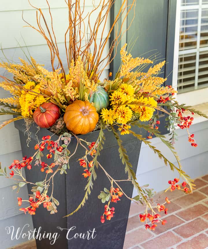 natural sticks, faux golden mums and multi colored pumpkins in a tall black urn