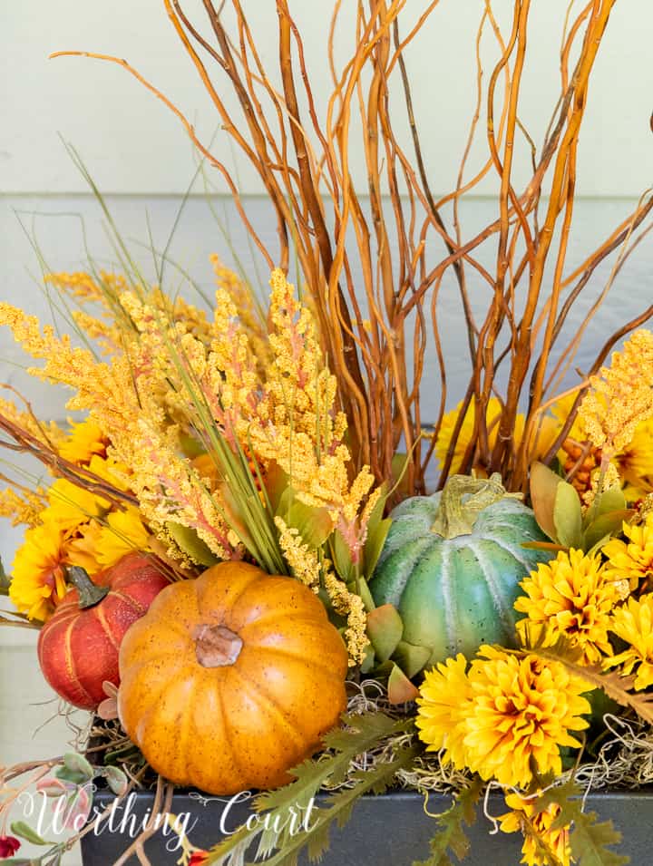 natural sticks, faux golden mums and multi colored pumpkins in the top of an urn