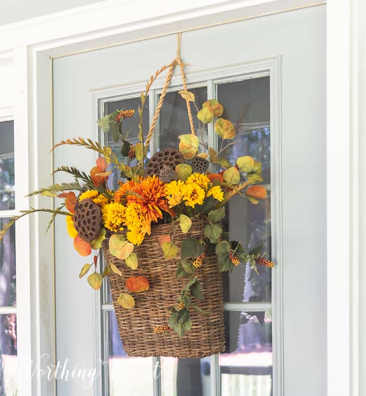 handing basket on gray front door filled with fall colored faux stems