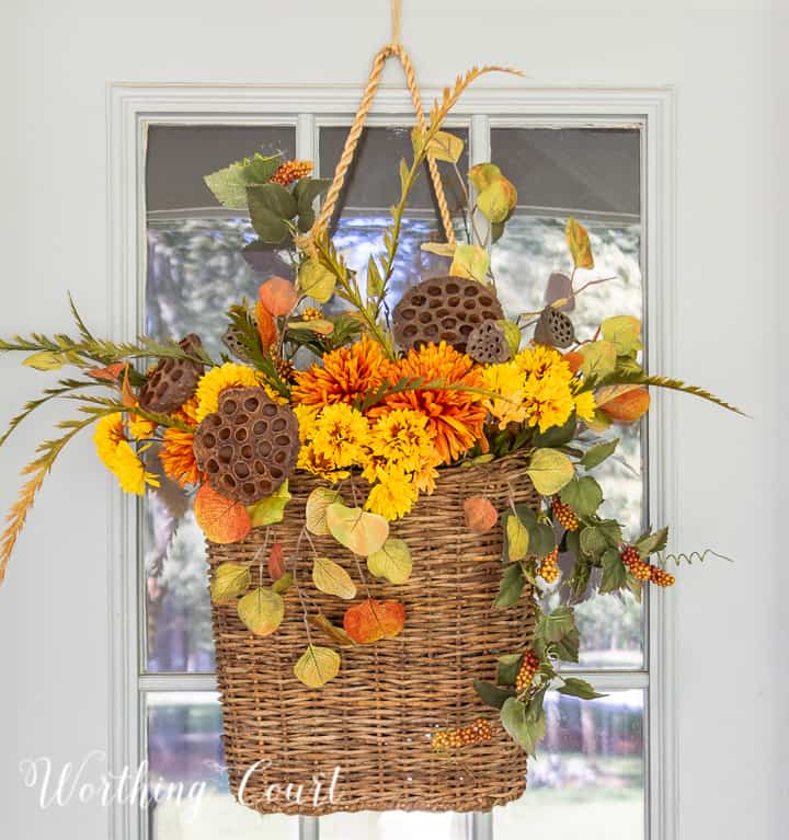 handing basket on gray front door filled with fall colored faux stems