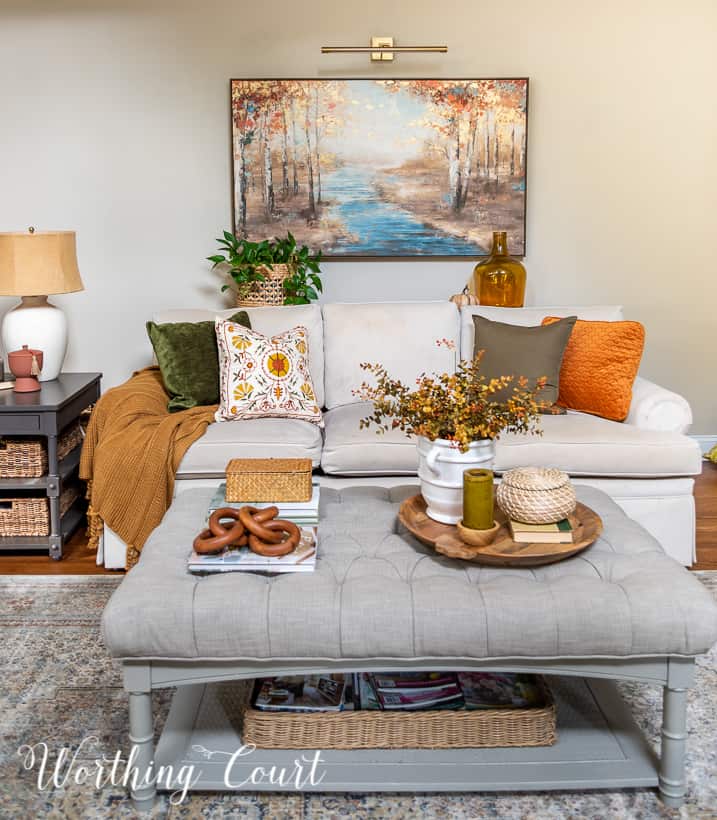 neutral colored couch filled with fall pillows with an upholstered coffee table in front