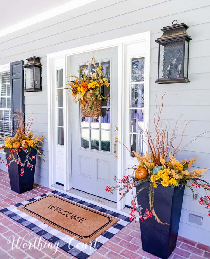 gray front door with a hanging basket and flanked with urns filled with faux fall stems and pumpkins in fall colors