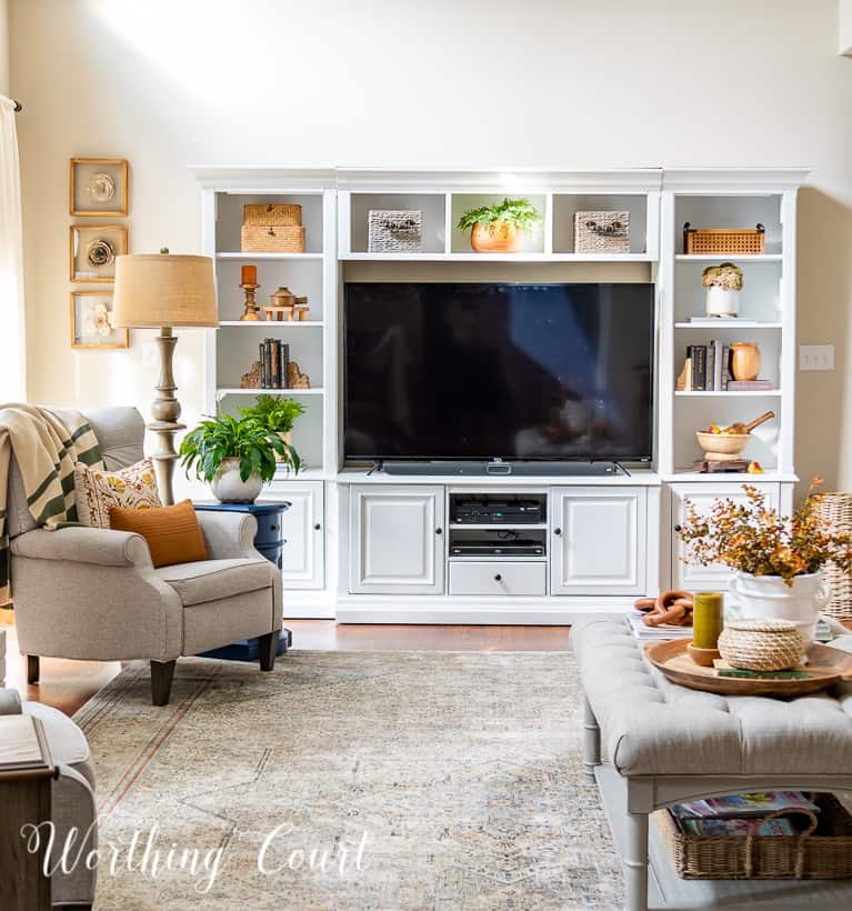 white entertainment center filled with tv and fall decor with a gray chair and coffee table in front