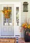 gray front door with a hanging basket and urn filled with faux fall stems and pumpkins in fall colors
