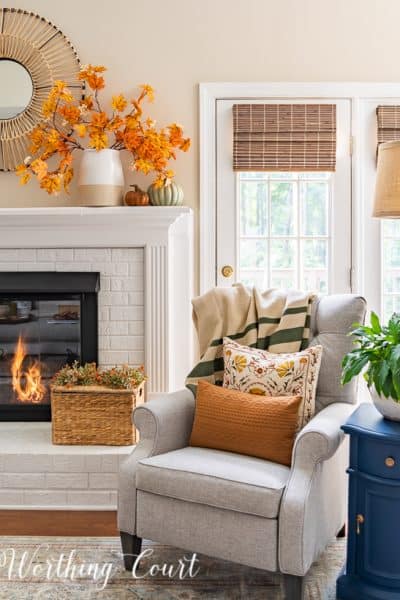 gray arm chair and side table beside white fireplace with fall decor on the mantel and hearth