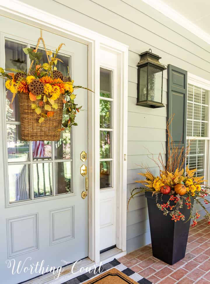 gray front door with a hanging basket and urn filled with faux fall stems and pumpkins in fall colors