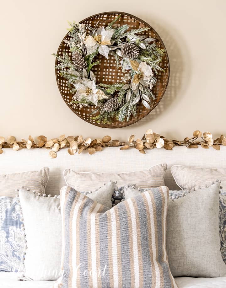 Christmas wreath hanging above upholstered headboard with a gold garland across the top