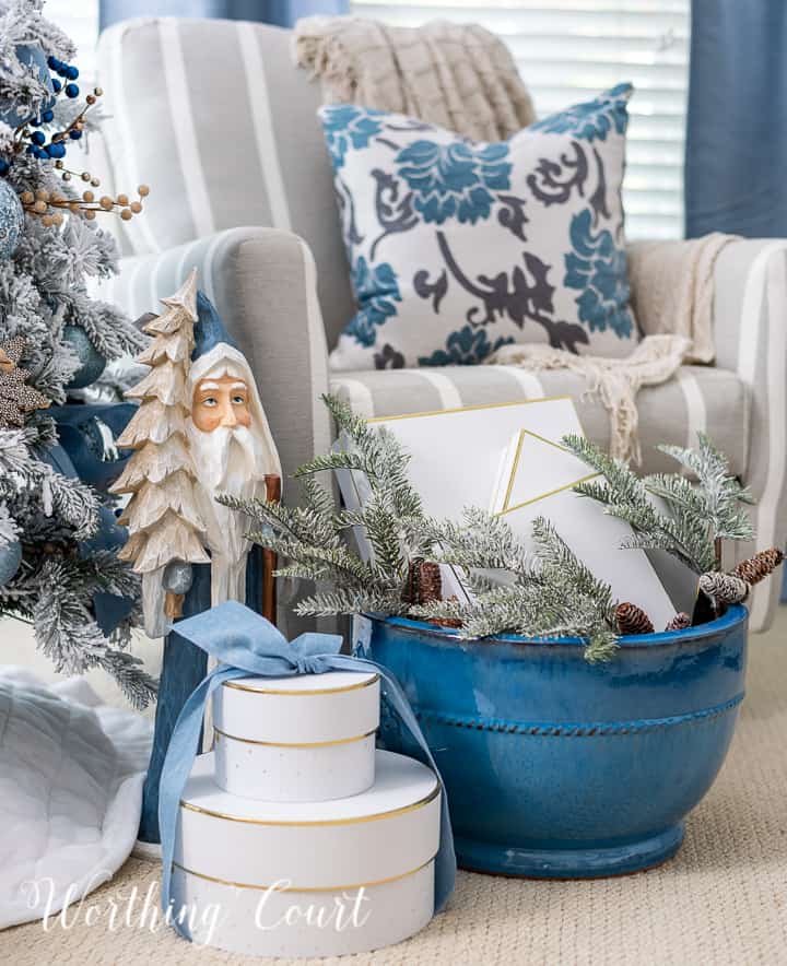 Blue Santa statue beside gifts under a Christmas tree