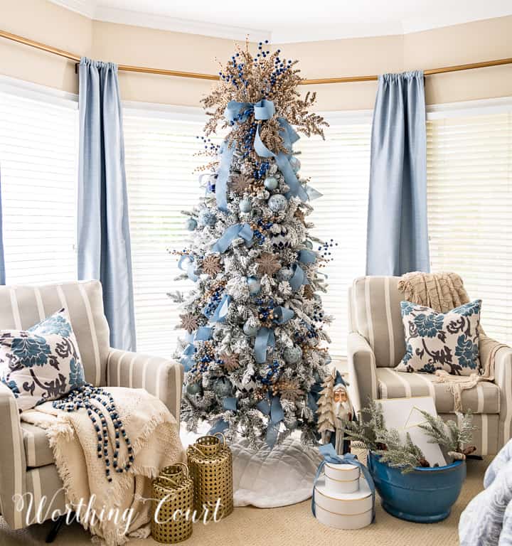 Flocked Christmas tree with blue and gold ornaments between two chairs